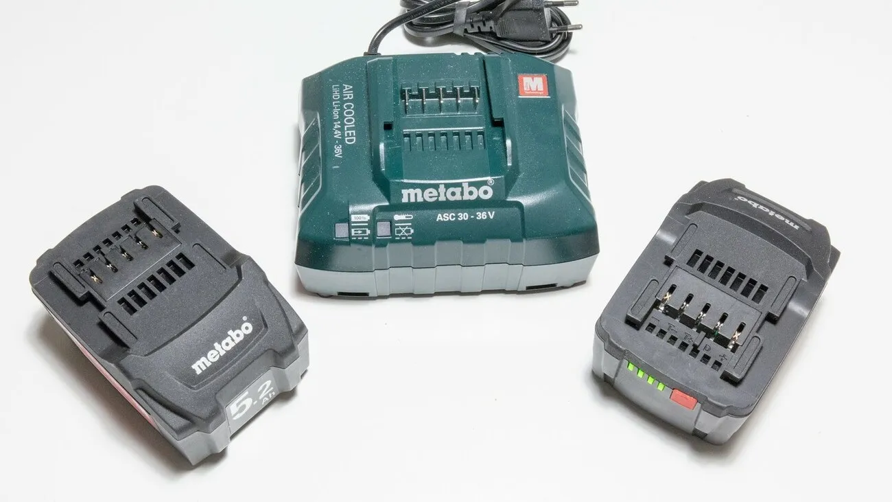 Zwei schwarze Akkus für den Metabo STA 18 LTX 140 liegen auf einer weißen Oberfläche. Dazwischen liegt das grüne Metabo Ladegerät für die Akkus.